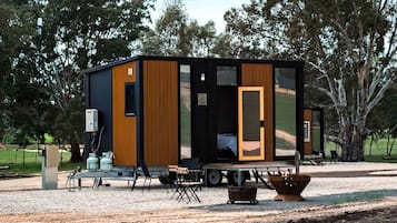 Una cabaña moderna y compacta con un amplio ventanal corredero, una pequeña zona de porche y suelo de grava.