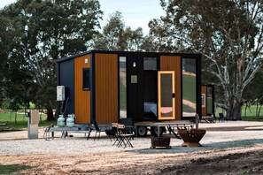 A modern, compact cabin with a large sliding door, a small porch area, and a gravel ground.