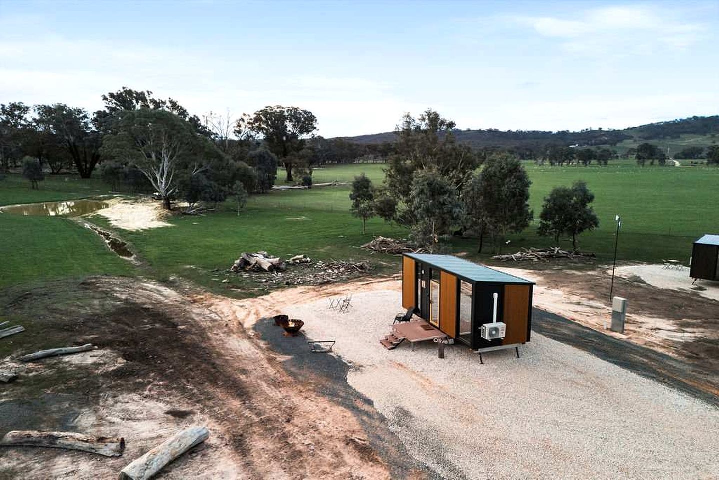 A small, single-story structure with a flat roof, situated on a gravel area with a dirt path leading to it.