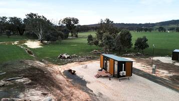 A small, single-story structure with a flat roof, situated on a gravel area with a dirt path leading to it.