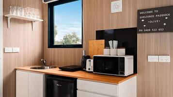A compact kitchen with a microwave, toaster, and a small sink. There's a window above the sink, and a welcome sign on the wall.