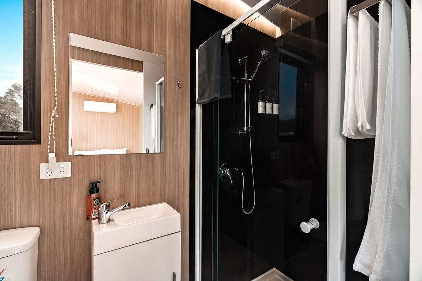 A modern bathroom with a glass shower enclosure, a white sink, and a mirror.