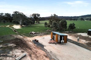 A small, single-story structure with a flat roof, situated on a gravel area with a dirt path leading to it.