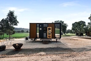 A modern cabin with a large sliding door, outdoor seating, and a fire pit.