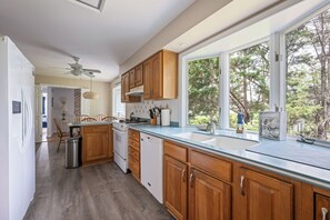 A modern kitchen with wooden cabinets, a stainless steel sink, and a large window offering a view of trees. - 3 Milford Avenue (7): 4  BR, 3  BA House in Lewes, Sleeps 10 (Lewes)