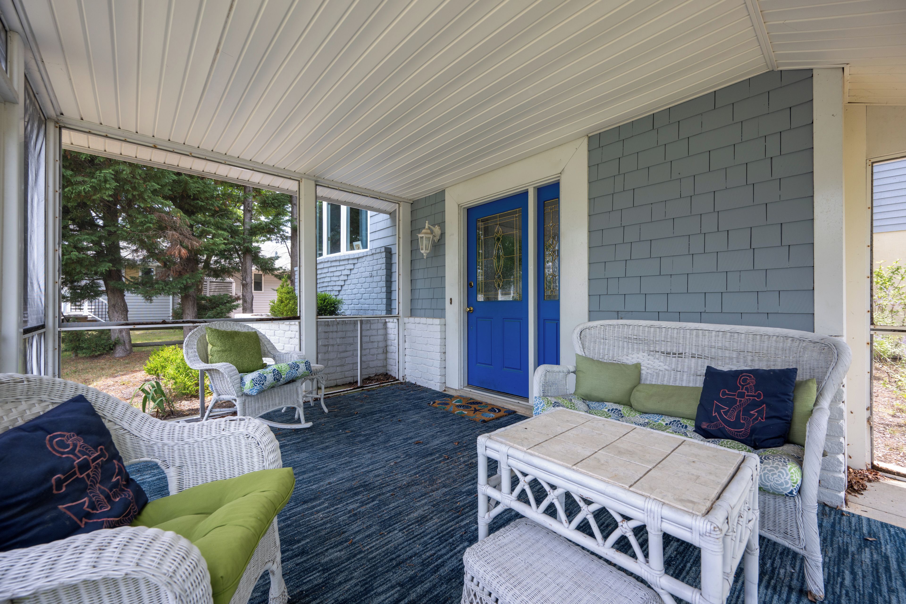 A covered porch with wicker furniture, a blue door, and a view of the outdoors.