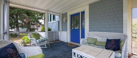 A covered porch with wicker furniture, a blue door, and a view of the outdoors.