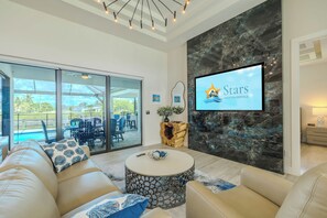 A modern living room with a large TV screen, comfortable seating, and a view of the outdoors. - New to the vacation rental, 4bed/3bath, hot tub and heated pool (Cape Coral)