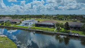 A residential area with houses along a canal, featuring a modern house with a large patio and a covered outdoor area. - New to the vacation rental, 4bed/3bath, hot tub and heated pool (Cape Coral)