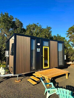 A small, modern cabin with a sliding door, a wooden table, and a bench. - Tiny House Retreat with Scenic Country Views in Numulgi, Australia (Numulgi)