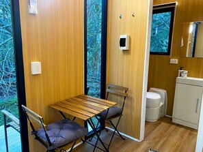 A compact room with a wooden table and two chairs, a small sink, and a window with a view of trees.