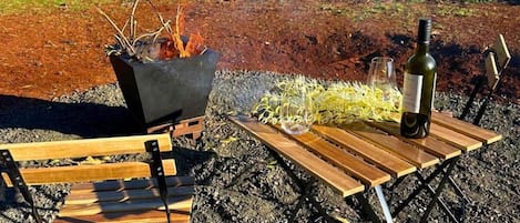Un espace extérieur aménagé avec un foyer, une bouteille de vin et un banc.