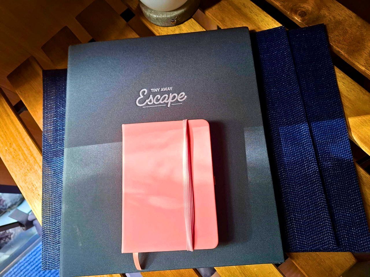 Una carpeta negra con el texto 'Tiny Away Escape', apoyada sobre una superficie de madera.