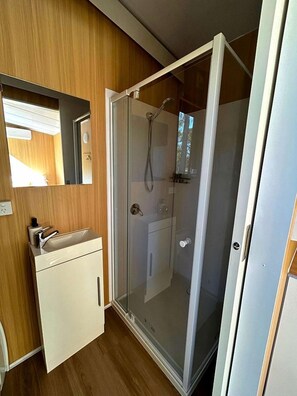 A compact bathroom with a shower enclosure, a mirror, and a sink.