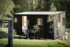A small, dark-colored cabin with a single visible room, a door, and a window.