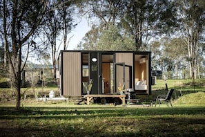 A small cabin with a sliding door, a dining table, and a chair outside.