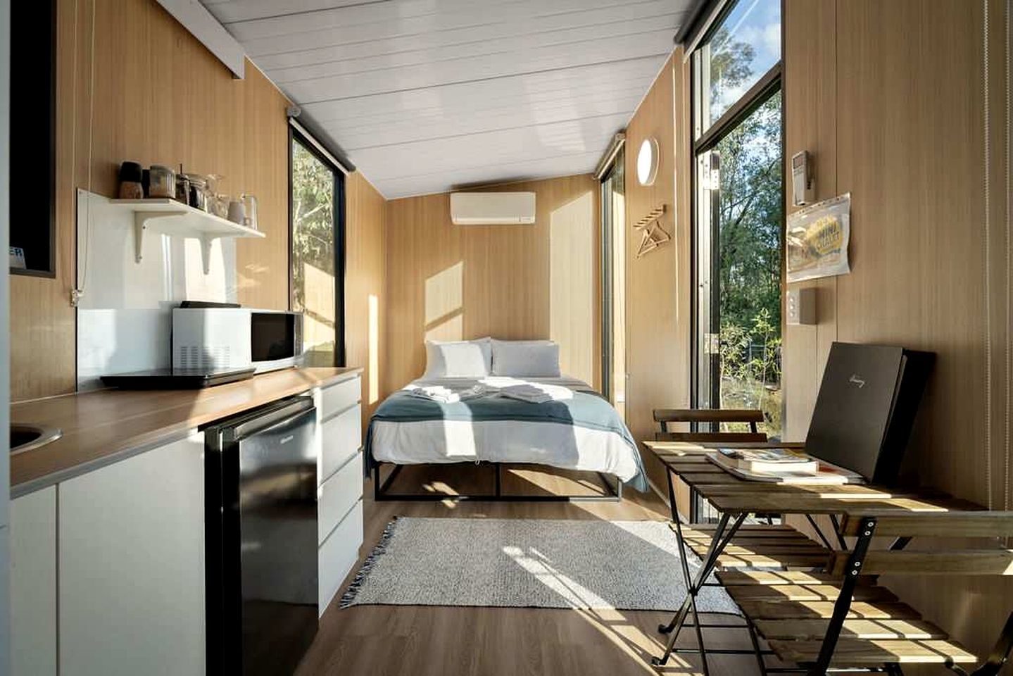Quarto compacto com cama, mesa de cabeceira e vista para o exterior.