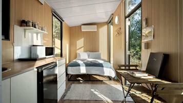 Quarto compacto com cama, mesa de cabeceira e vista para o exterior.