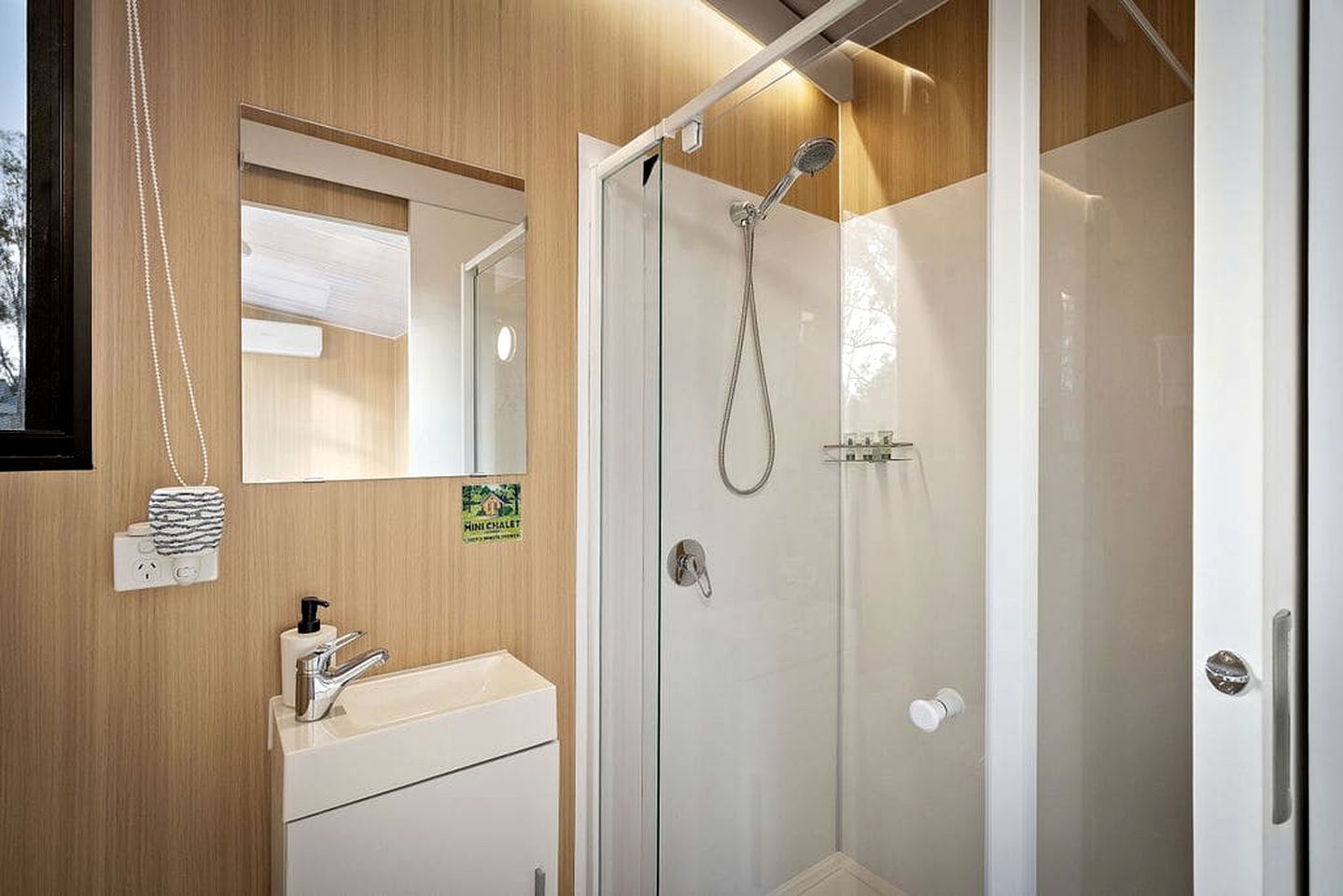 Casa de banho moderna com chuveiro em cabine de vidro, lavatório branco e espelho.