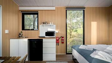 A modern bedroom with a bed, a small kitchenette with a microwave, and a view of the outdoors.