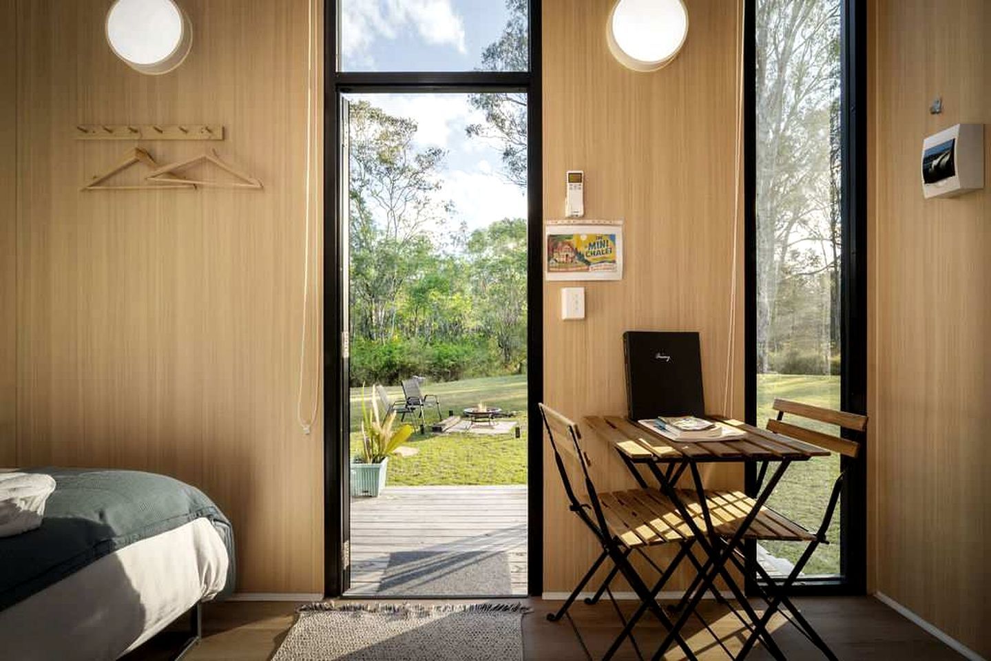 Een kamer met een bed, een eettafel met stoelen, een klein zwart kastje en uitzicht op een tuin door een glazen deur.