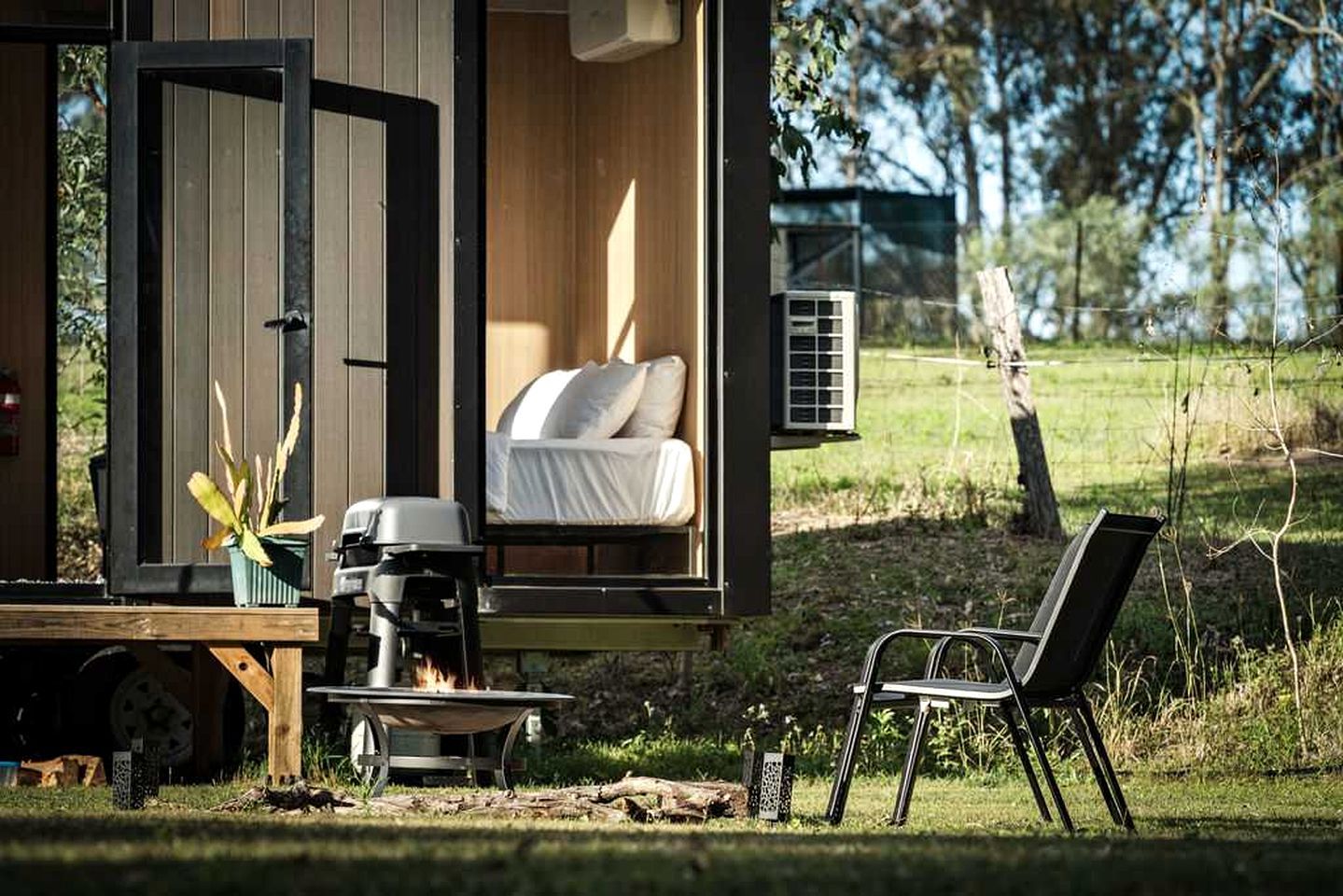 A cozy outdoor sleeping area with a bed, a grill, and a chair.