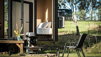 A cozy outdoor sleeping area with a bed, a grill, and a chair.