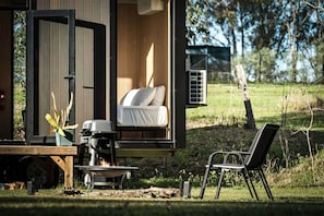 A cozy outdoor sleeping area with a bed, a grill, and a chair.
