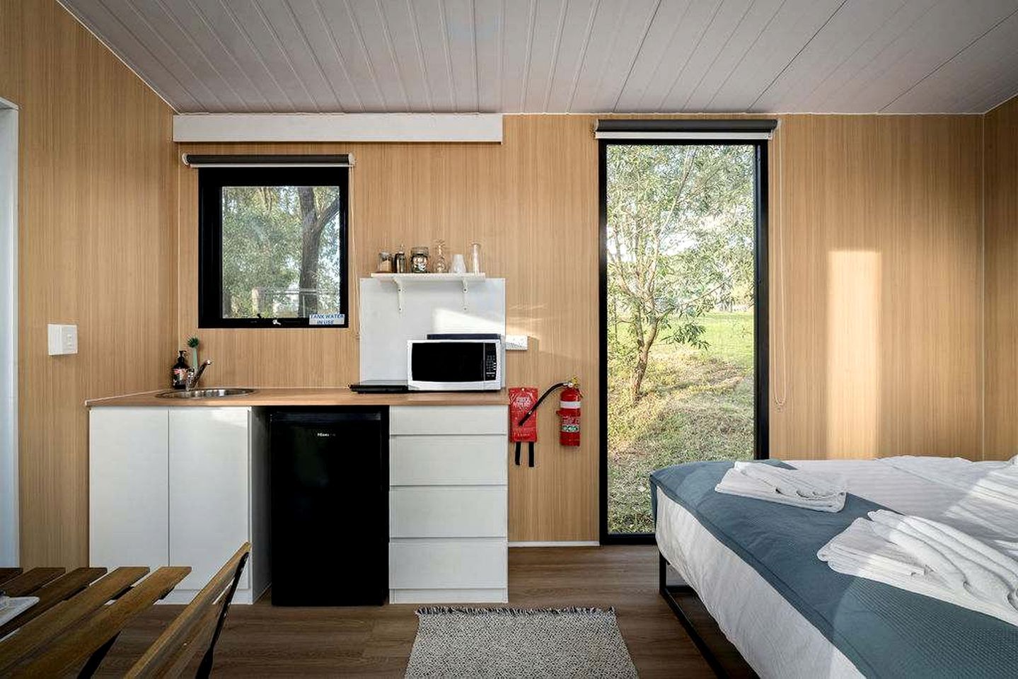 A modern bedroom with a bed, a small kitchenette with a microwave, and a view of the outdoors.