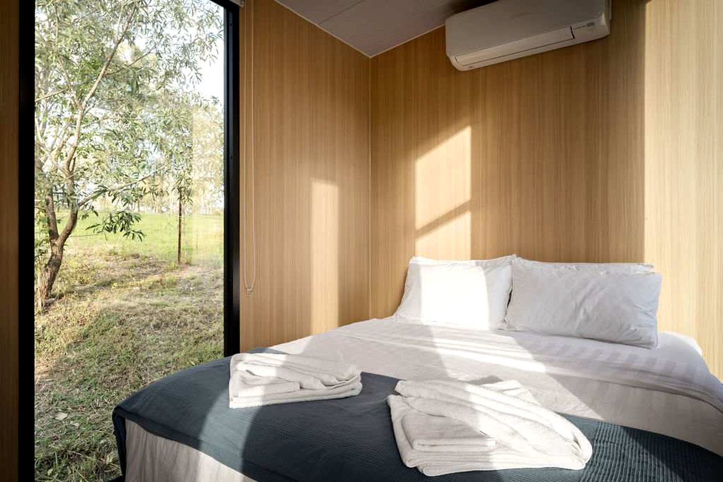 Un dormitorio con cama, almohadas y ventana con vista a un área verde.