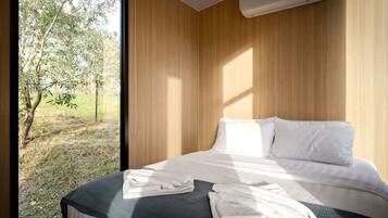Un dormitorio con cama, almohadas y ventana con vista a un área verde.