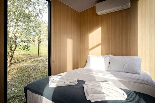 A bedroom with a bed, pillows, and a window overlooking a grassy area.