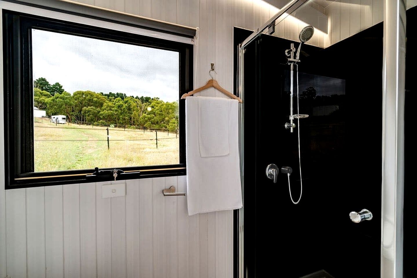 A bathroom with a window, a towel hanging on a rack, and a shower with a control panel.