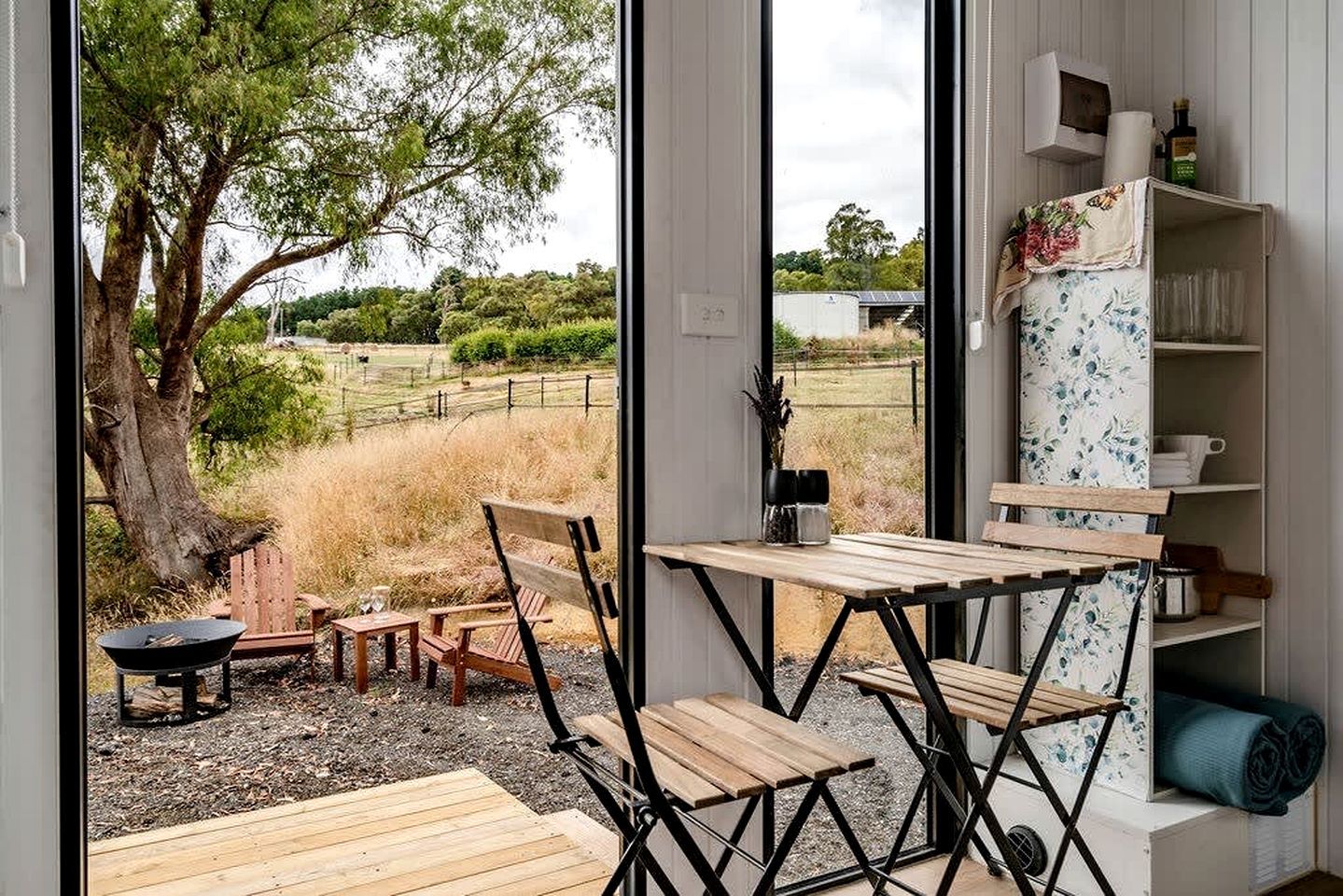 Une pièce dotée d’une grande fenêtre, d’une table en bois, de chaises, d’un petit foyer et d’une bibliothèque agrémentée d’objets décoratifs.