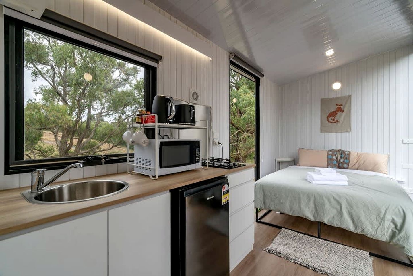 Habitación compacta con cama, kitchenette pequeña con microondas y ventana con vista a árboles.