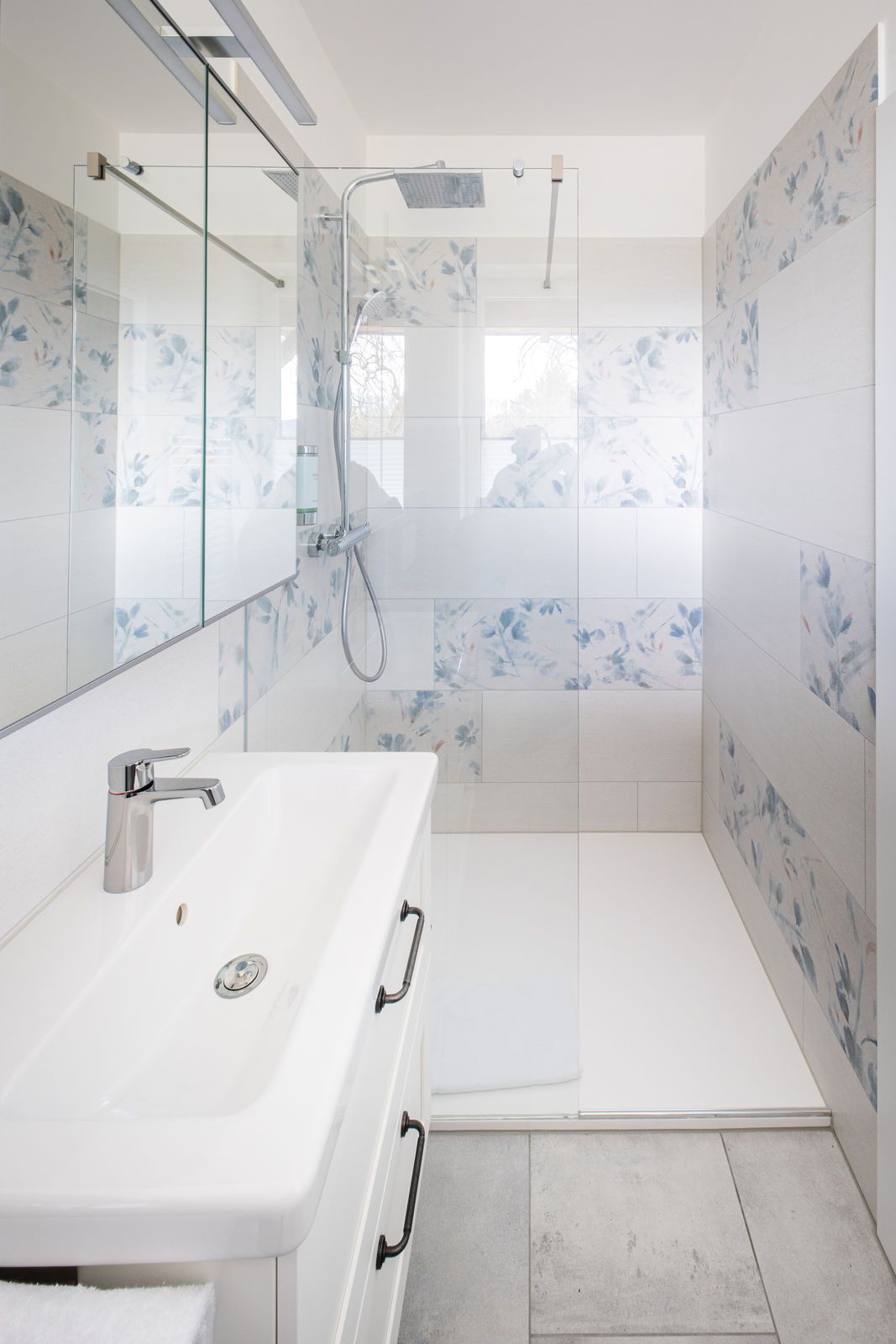 Une salle de bain moderne avec un lavabo blanc, une cabine de douche en verre et une zone de douche carrelée.