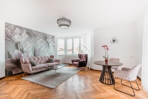 A modern living room with a sofa, armchairs, a coffee table, and a dining table. There is a large floral mural on the wall, a floor lamp, and a ceiling light fixture. - Hotel Magnolie GmbH (Laufenburg)
