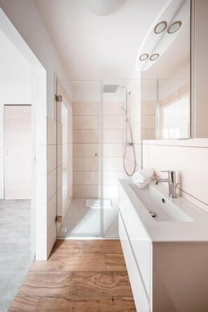 A modern bathroom with a glass shower enclosure, a white sink, and a large mirror. - Hotel Magnolie GmbH (Laufenburg)