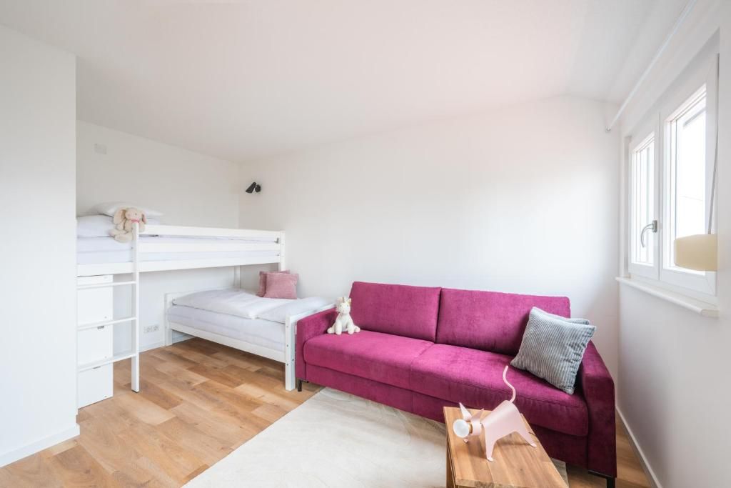 Ein Zimmer mit einem Etagenbett, einem rosafarbenen Schlafsofa, einem kleinen Tisch und einem Fenster.