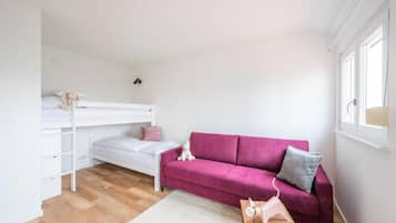 Ein Zimmer mit einem Etagenbett, einem rosafarbenen Schlafsofa, einem kleinen Tisch und einem Fenster.