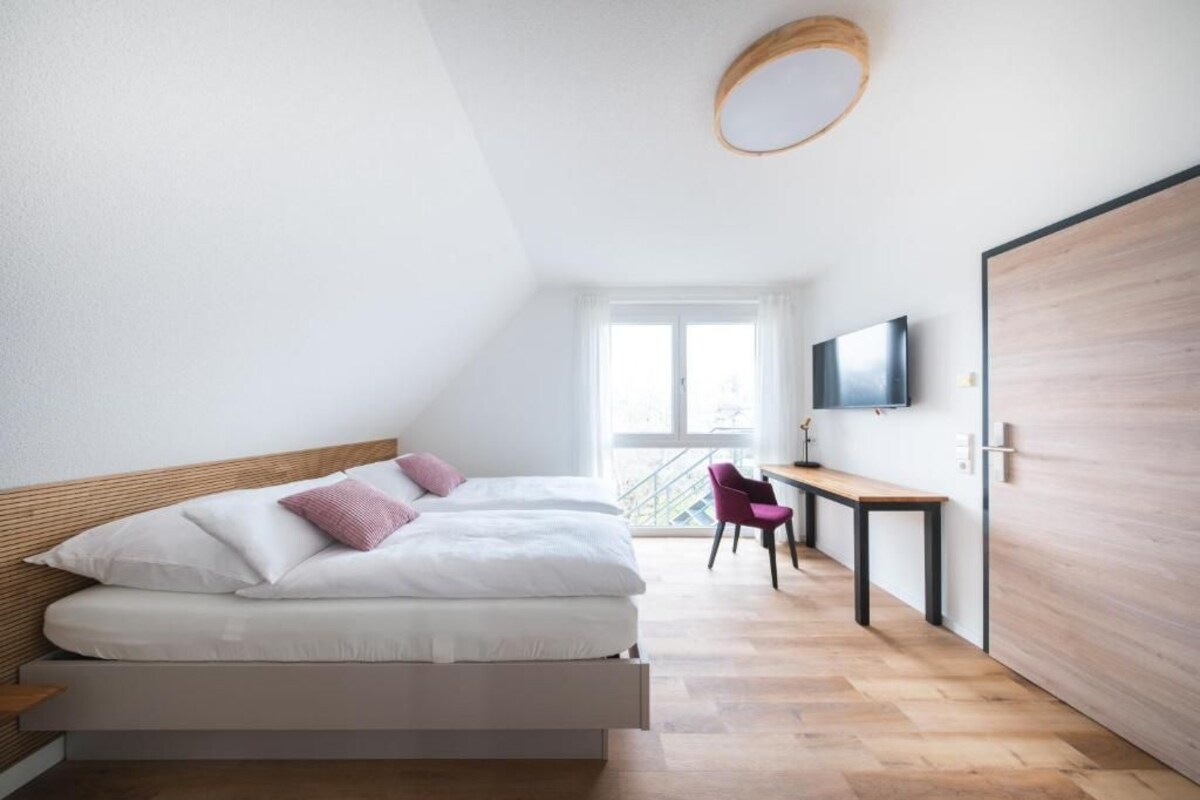 A modern bedroom with a bed, a desk, a chair, and a television.
