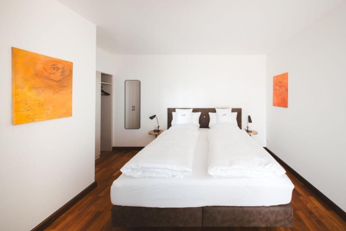 A hotel room with a large bed, a wardrobe, a mirror, and two paintings on the walls.
