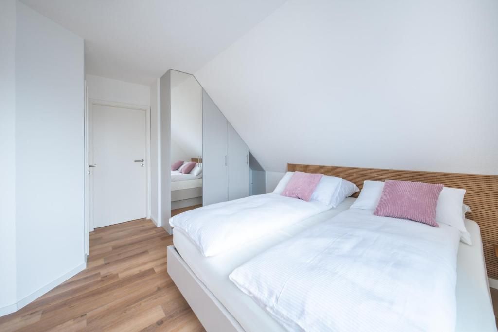 A bedroom with a sloped ceiling, a bed with white bedding, a wooden headboard, and a mirror reflecting the room.