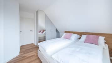A bedroom with a sloped ceiling, a bed with white bedding, a wooden headboard, and a mirror reflecting the room.