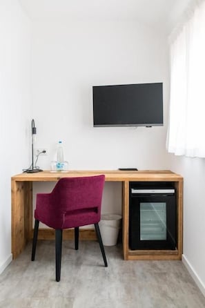 A room with a wooden desk, a purple chair, a television mounted on the wall, and a small window.