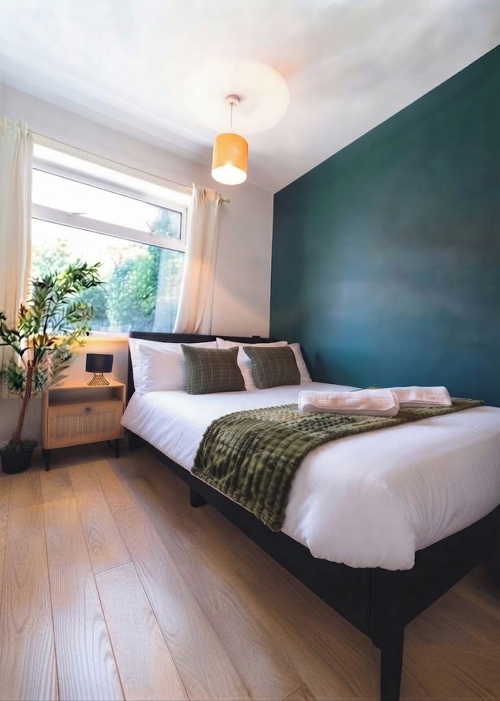 A bedroom with a bed, bedside table, lamp, and a window with curtains.