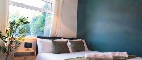 A bedroom with a bed, bedside table, lamp, and a window with curtains.