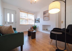 A living room with a sofa, a coffee table with a bottle and glasses, a floor lamp, and a fireplace. - Cosy 2-Bed Home in Mansfield  (Mansfield)
