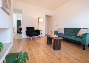 A living room with a green sofa, a black armchair, a small table with a vase, and a floor lamp. - Cosy 2-Bed Home in Mansfield  (Mansfield)