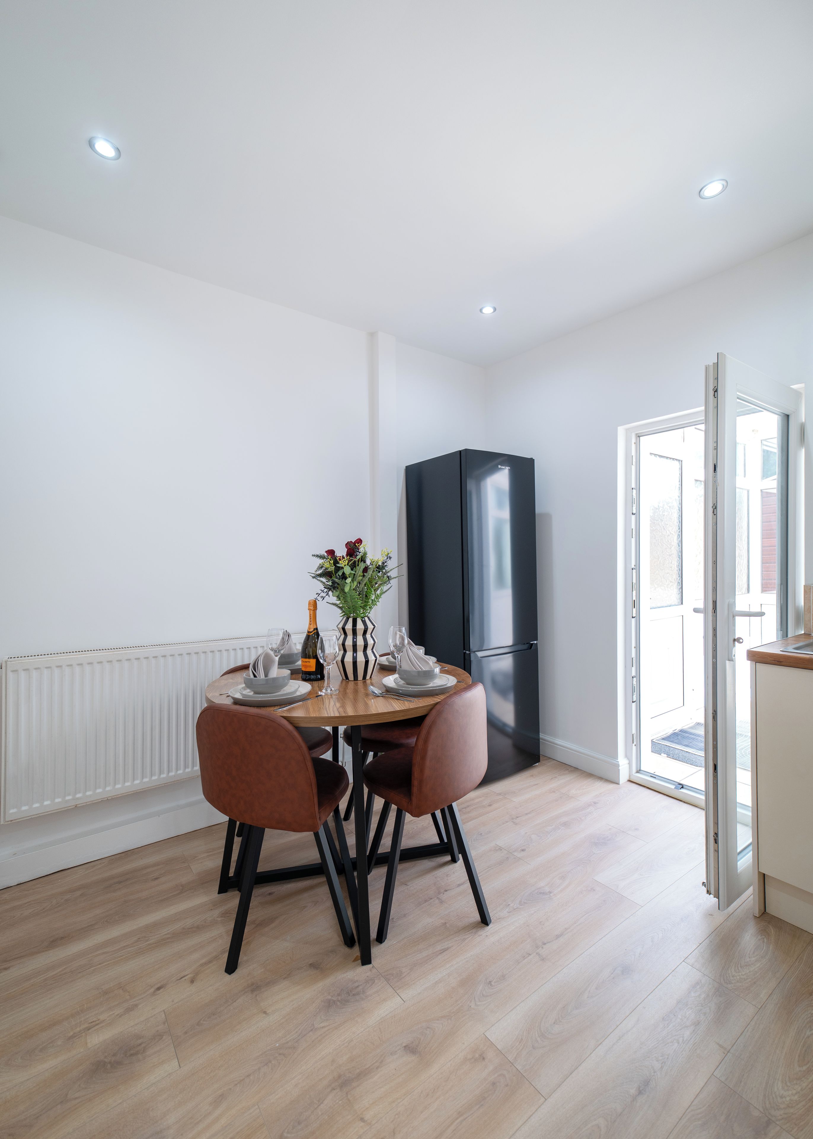 A modern kitchen with a black refrigerator, a dining table with chairs, and a white radiator.
